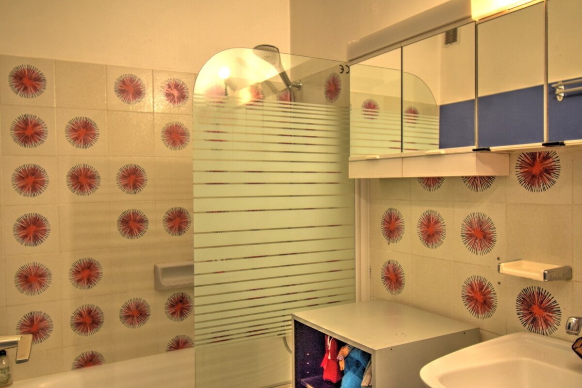 A retro bathroom with orange starburst patterned tiles, a frosted glass shower screen, mirrored cabinets, and a sink.