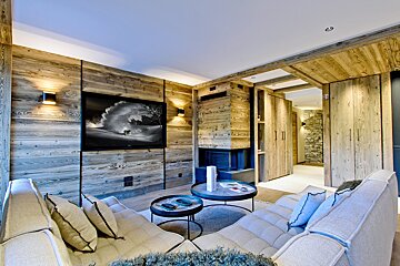 Cozy, modern living room with rustic wood paneling, a large TV, a built-in fireplace, and comfy sofas around round coffee tables.