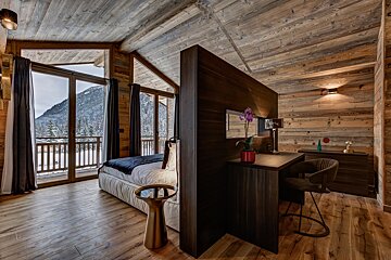 A bedroom with a bed and a desk with a view of the mountains