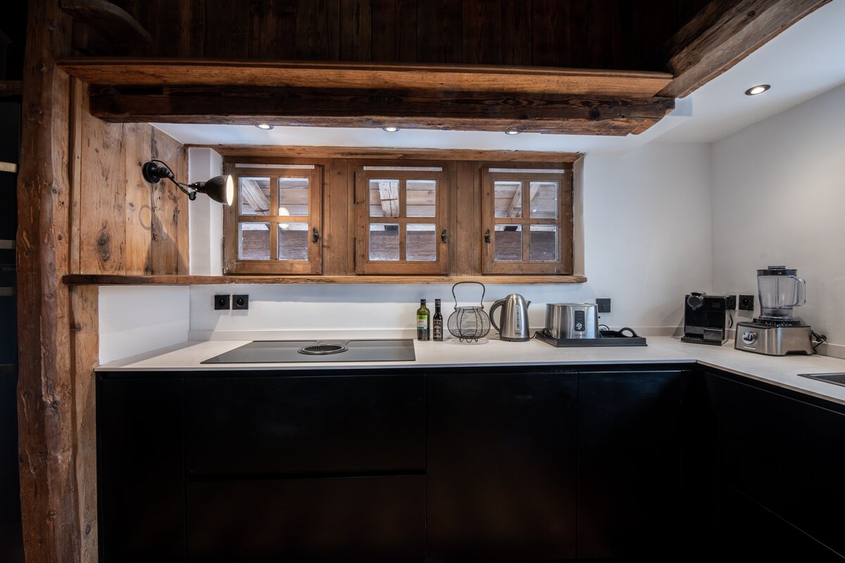 Modern kitchen with black cabinets and white countertops, accented by rustic wood paneling and three small windows.