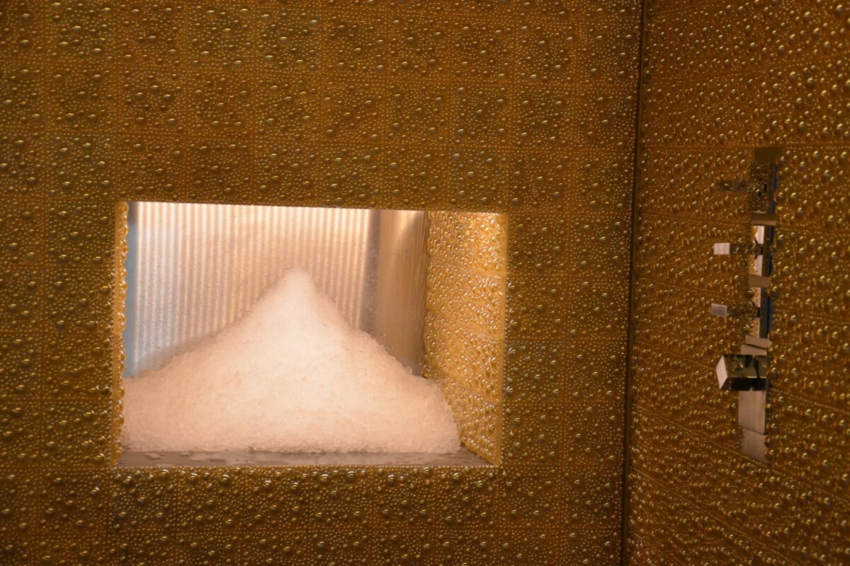 A golden, bubble-textured wall features a recess filled with white crushed ice, next to a metallic control panel or fixture.
