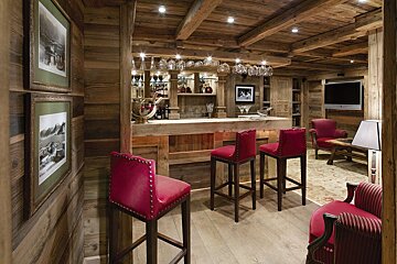 A wooden room with a bar and red chairs
