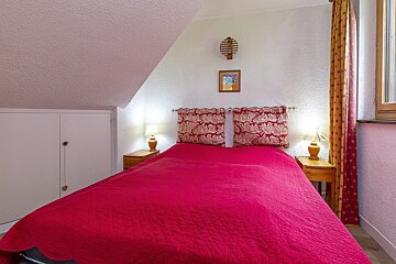 A bed with a red blanket and a picture on the wall above it