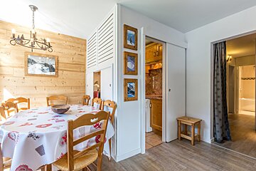 Rustic chalet dining room with wood-paneled walls, an oval table, wooden chairs, a chandelier, and glimpses of a kitchen and hallway.