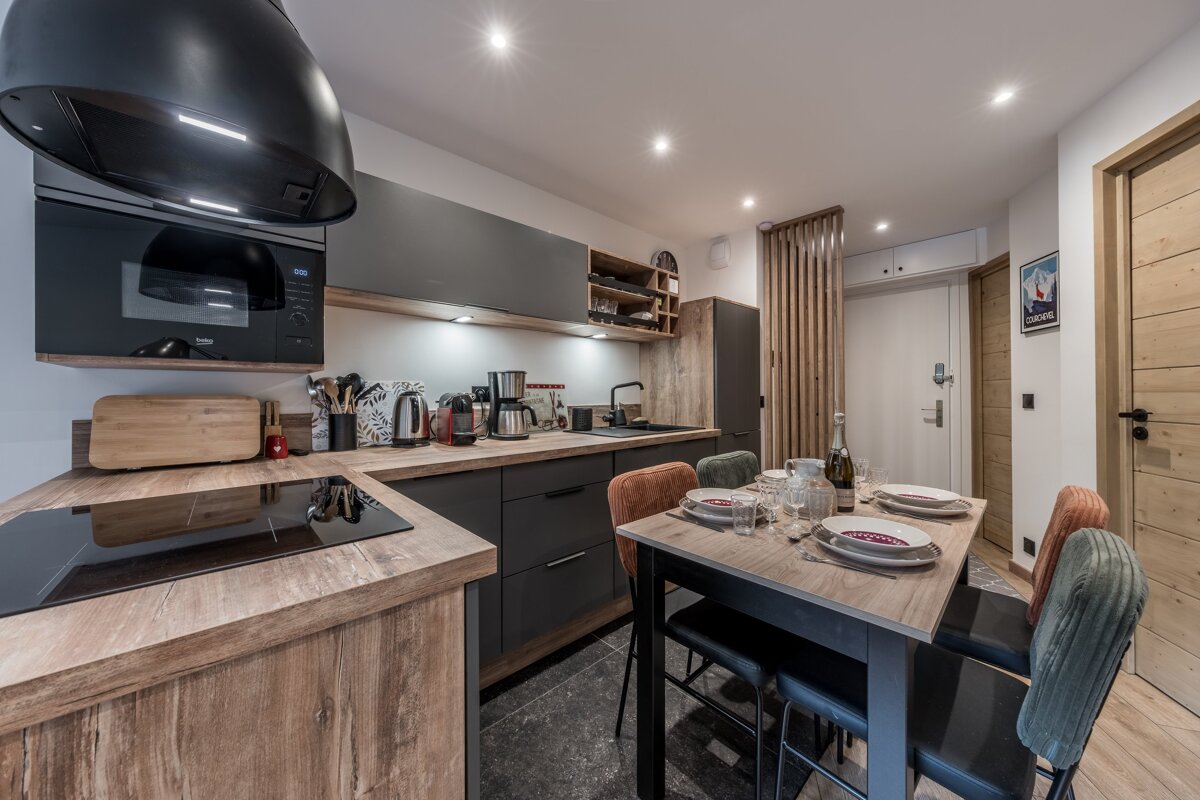 A modern kitchen and dining area with dark cabinets, wood accents, and a set dining table, creating a contemporary and inviting space.