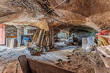 A dusty, old stone cellar with low vaulted ceilings, cluttered with wooden planks, crates, and storage items.