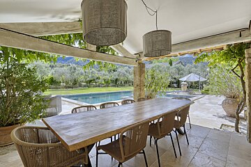 A wooden table and chairs on a patio with a pool in the background