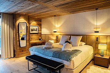 Luxurious, cozy bedroom with wooden walls and ceiling, a large bed with white robes, modern lighting, and a full-length mirror.