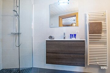 Clean, modern bathroom with a glass shower stall, a dark wood floating vanity, a mirror, and a white heated towel rack.
