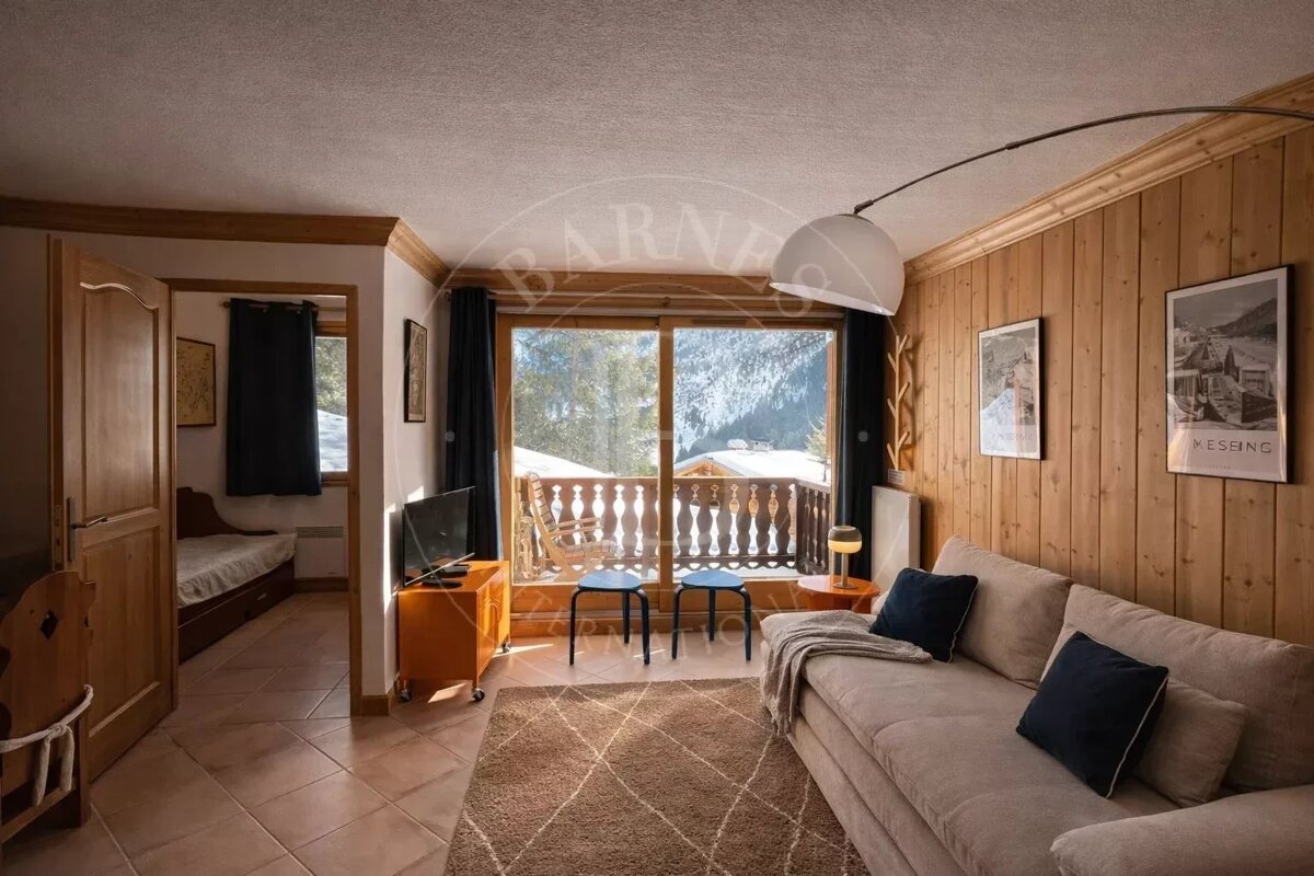 Cozy alpine living room with wood paneled walls, a sofa, and sliding glass doors opening to a snowy balcony view.