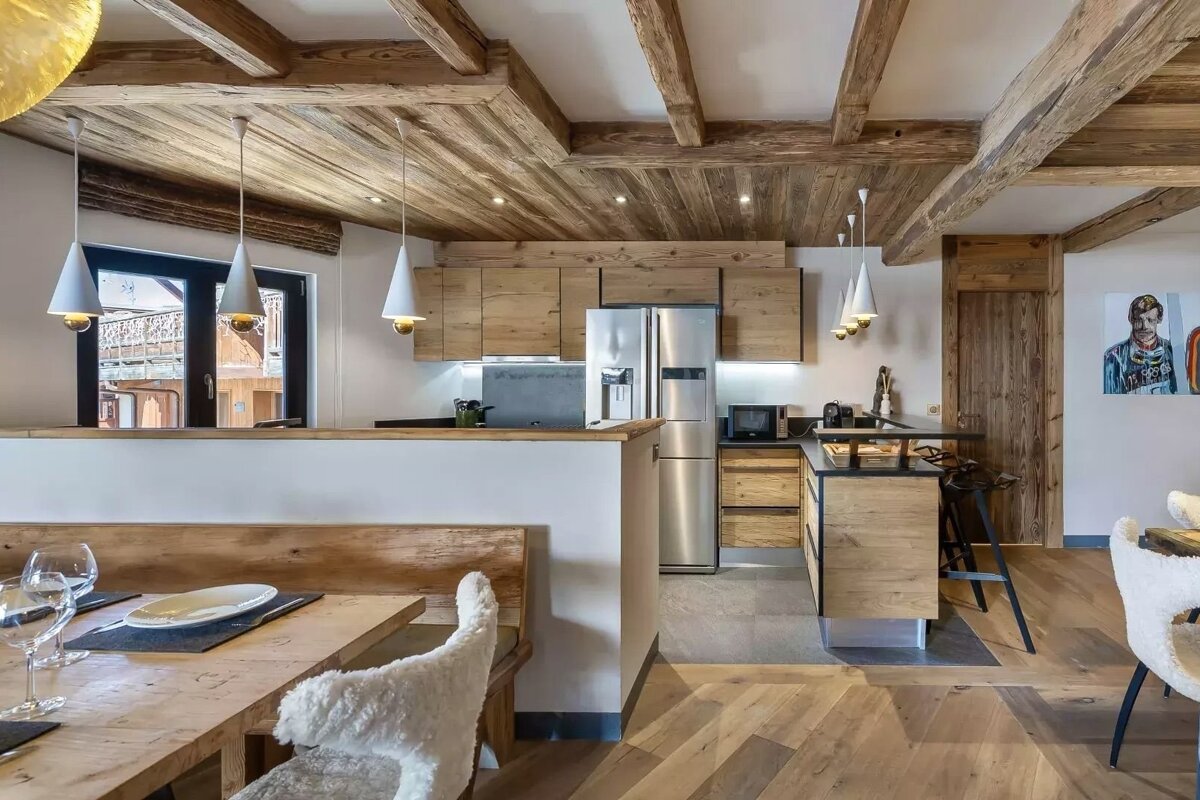 A rustic-modern kitchen and dining space with exposed wooden beams, natural wood cabinetry, stainless steel appliances, and cozy seating.
