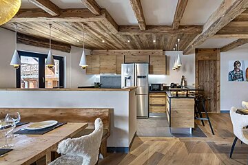 A rustic-modern kitchen and dining space with exposed wooden beams, natural wood cabinetry, stainless steel appliances, and cozy seating.