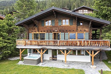 A large wooden chalet with a hot tub in front of it
