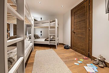 A children's room features two white bunk beds, warm wooden floors, a wooden door, and scattered toys, including a teddy bear.