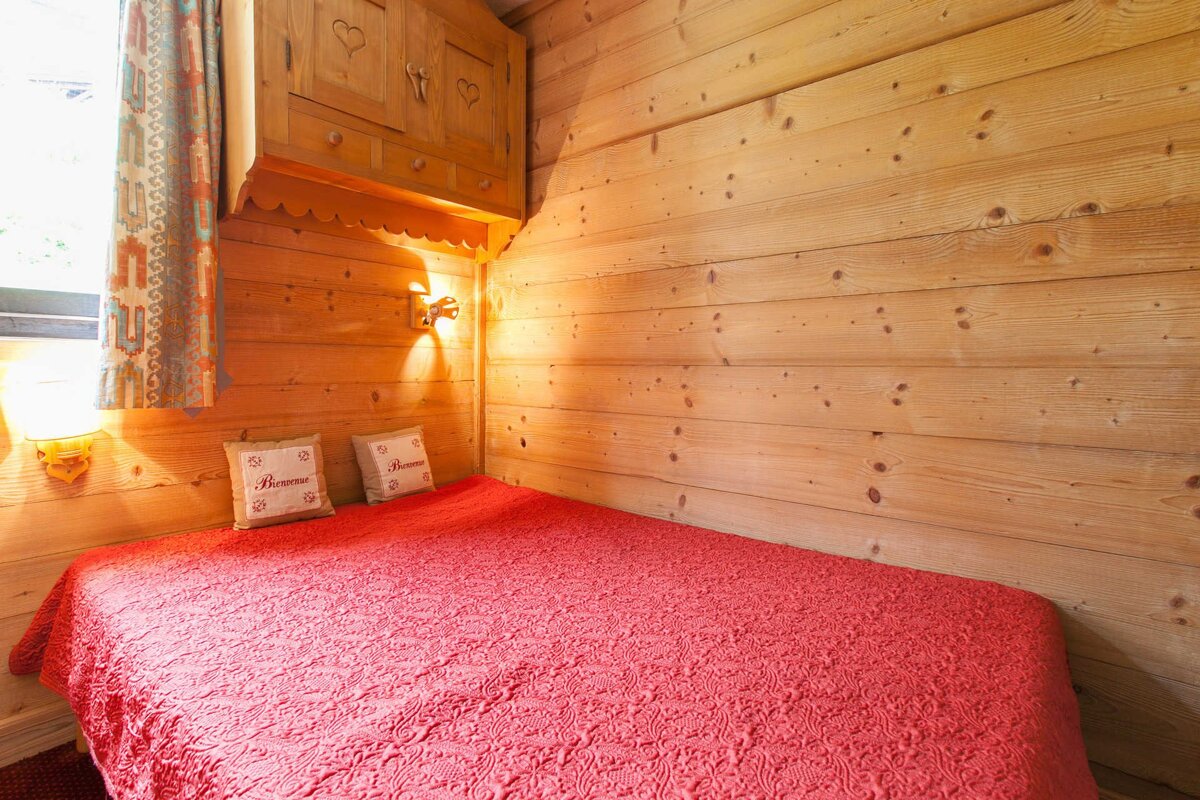 Rustic wood-paneled bedroom featuring a red quilted bed with 