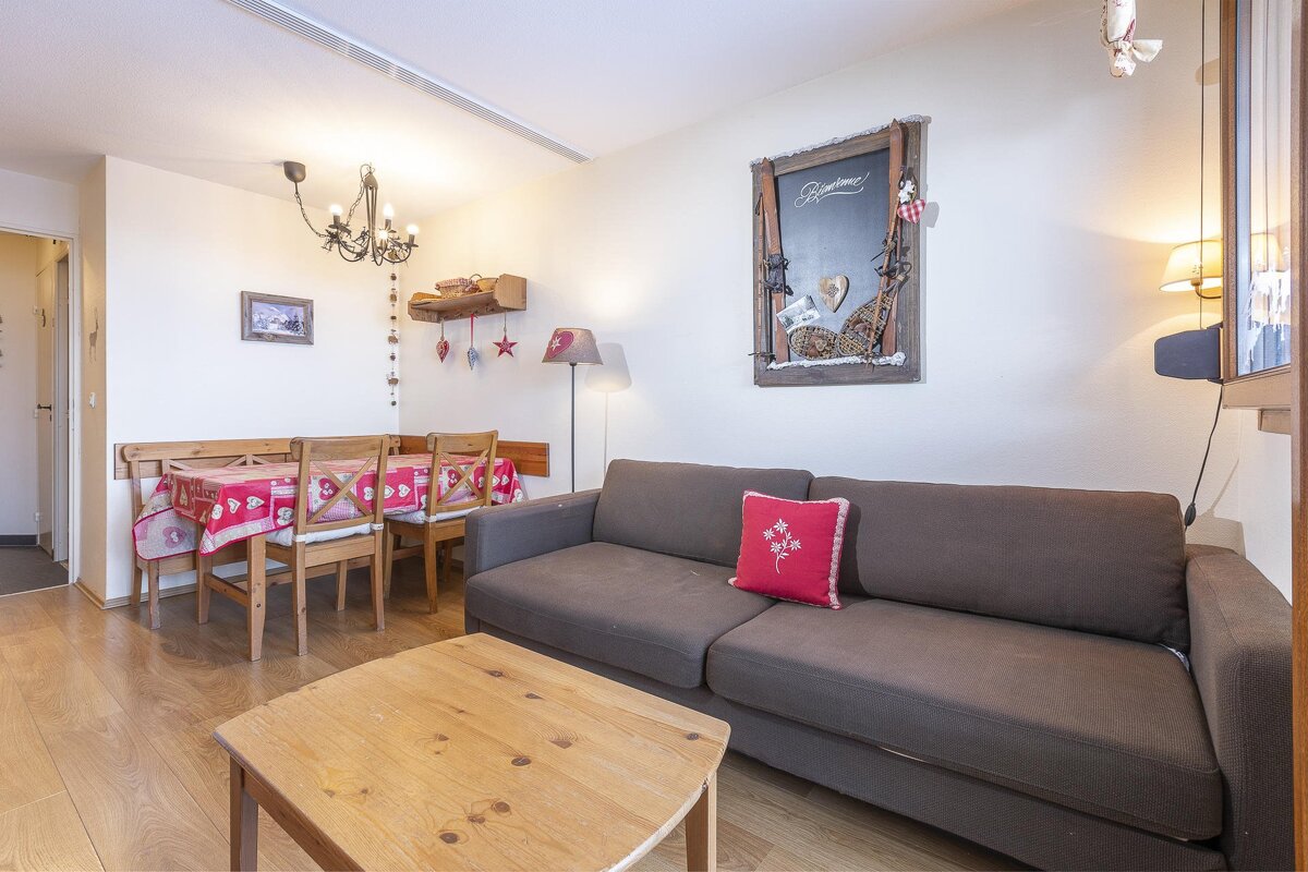 A cozy, ski-themed living/dining room features a brown sofa, wooden coffee table, and a dining set with a red tablecloth. Alpine decor adorns the walls.