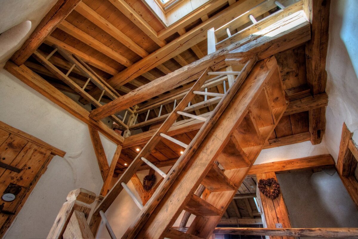 A wooden staircase with a ladder going up to the second floor