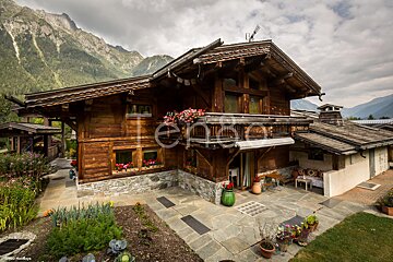 A large wooden house with mountains in the background is for sale