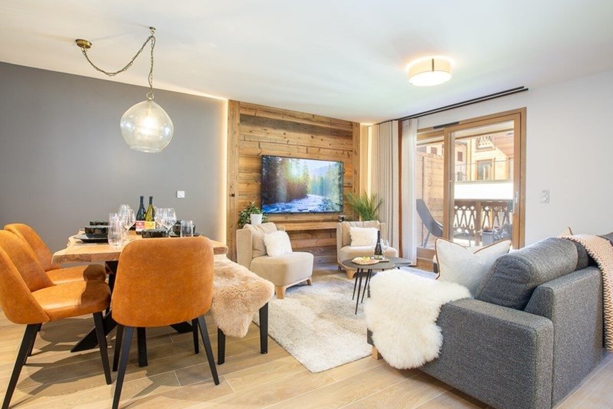 Cozy, modern apartment interior with a dining table, orange chairs, and a living area featuring a rustic wood accent wall and grey sofa.