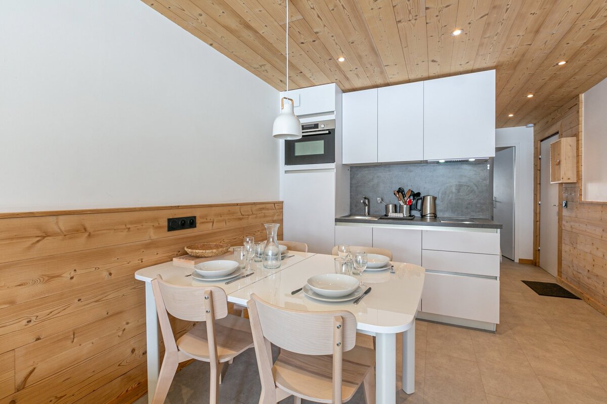 Bright, modern kitchen-diner with white cabinets, wooden walls/ceiling, and a white dining table set with place settings.