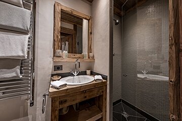 Cozy rustic bathroom featuring a wooden vanity, matching mirror, towel warmer, and a glass-walled shower with grey mosaic tiling.