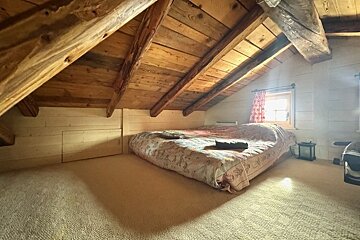 Cozy attic bedroom with a slanted wooden beam ceiling, carpeted floor, and a mattress on the floor near a small window.