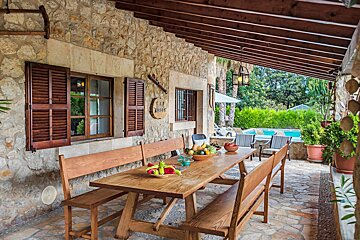 A wooden table with a bowl of fruit on it sits under a wooden roof