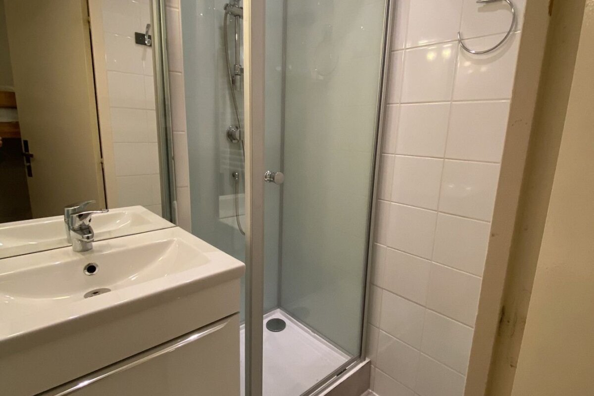 A clean, modern bathroom featuring a white sink with a chrome faucet next to a glass-enclosed shower stall.