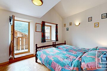 A cozy bedroom with two twin beds, a balcony offering mountain views, a window with curtains, and pictures adorning the wall.
