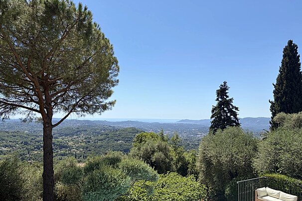 A scenic, elevated view of rolling hills, trees, and the distant coastline under a clear blue sky.