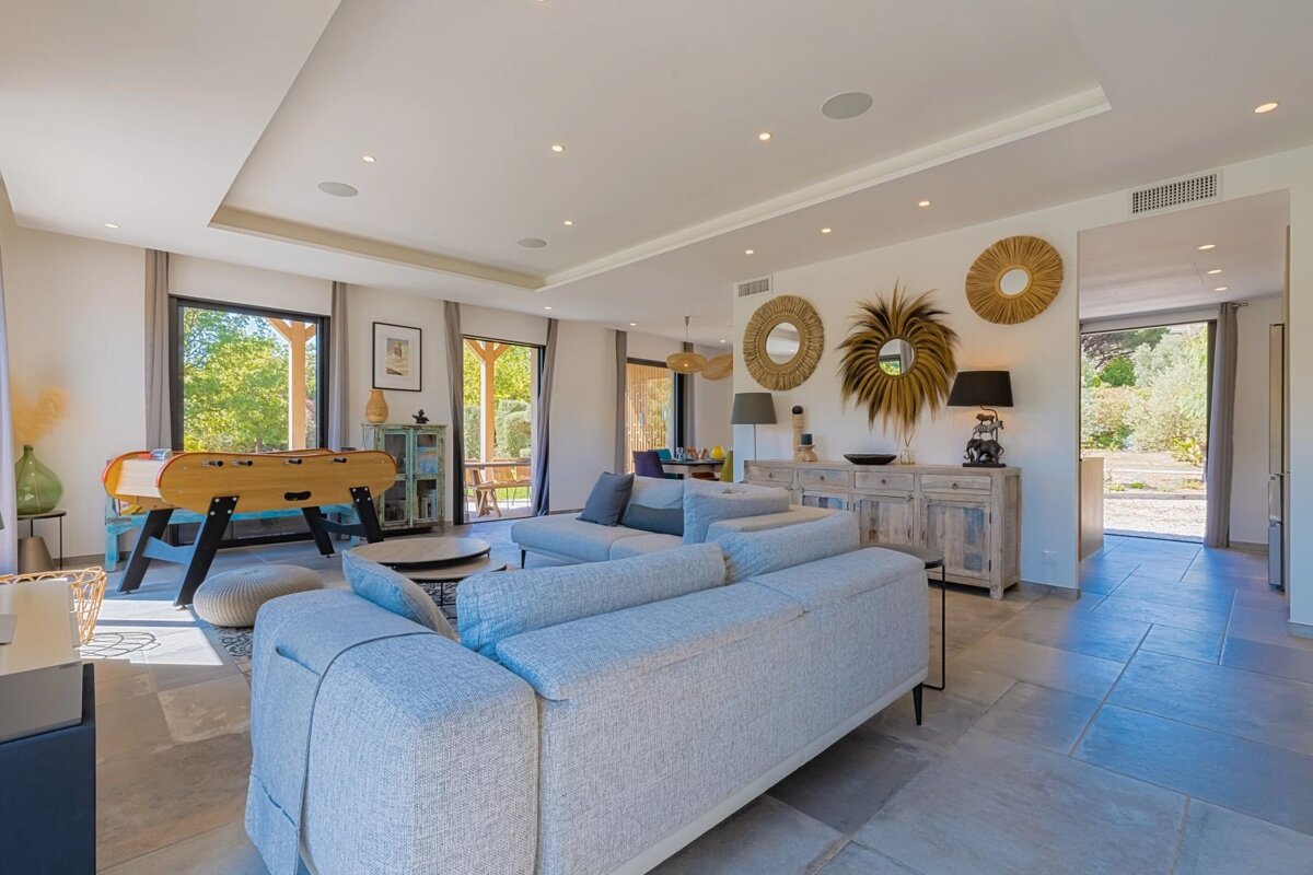 Spacious, modern living room featuring light gray sofas, tiled flooring, a foosball table, and stylish, bohemian-inspired wall decor.