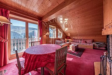 Rustic wood chalet room with red carpet & decor, mountain view balcony, dining table, sofa, and fireplace.
