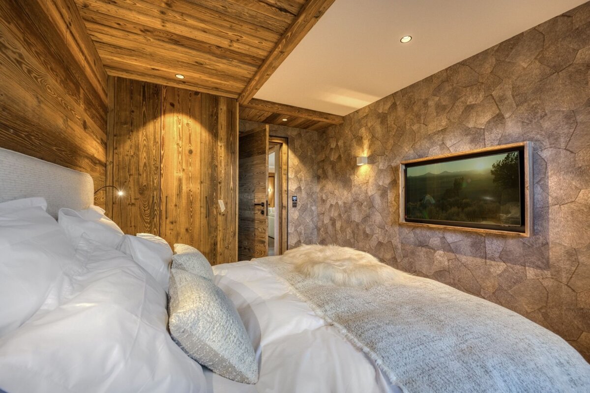 Rustic-chic bedroom with warm wooden walls/ceiling, a textured stone accent wall with a TV, and a plush white bed.