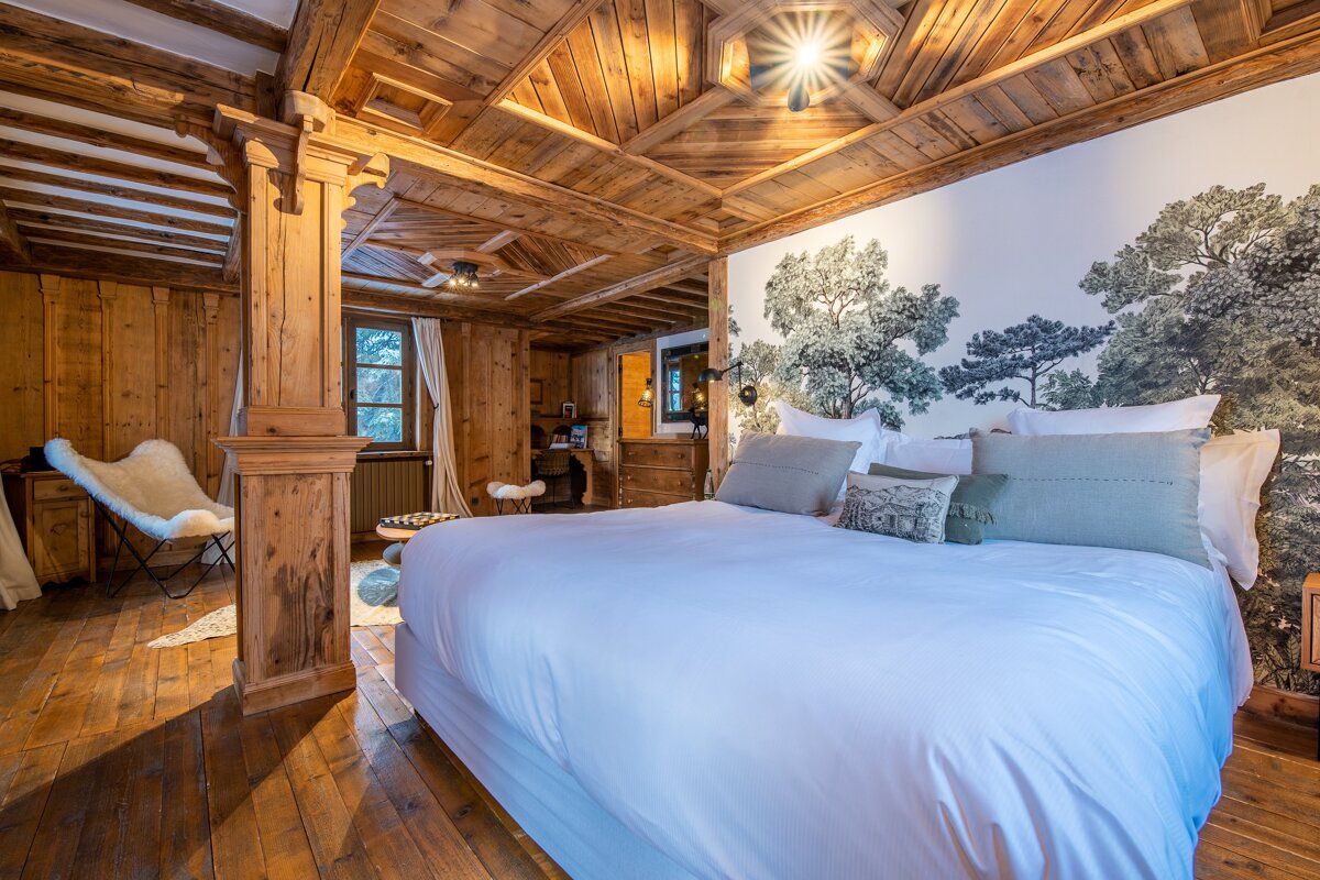 Rustic chalet bedroom featuring a wooden ceiling and walls, a large bed, and a forest tree mural behind the headboard.