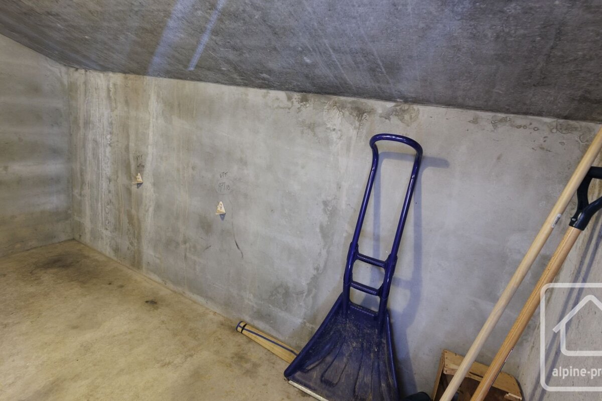 A bare concrete room with a blue snow shovel and other tools leaning against the wall.
