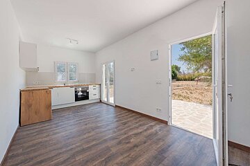 Bright, minimalist kitchen with white cabinets, dark wood floor, and open doors leading to a dry garden patio.