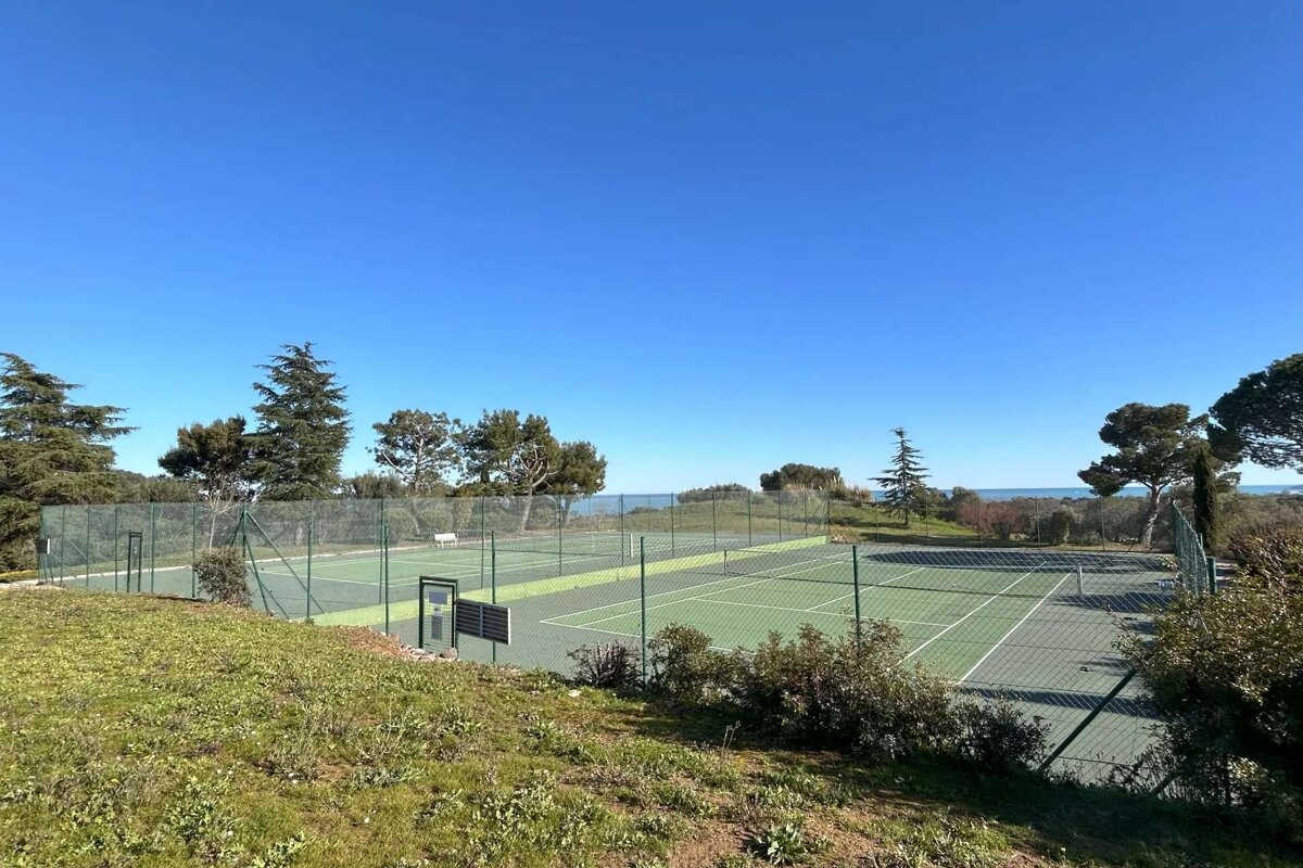 A tennis court is surrounded by a fence and trees