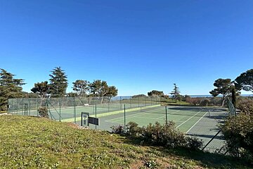 A tennis court is surrounded by a fence and trees