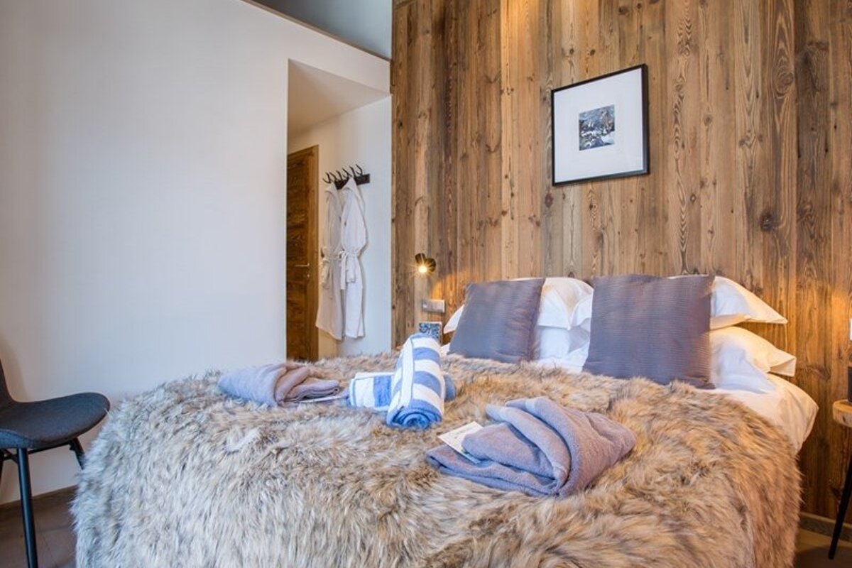 Cozy chalet bedroom featuring a bed with a fluffy faux-fur blanket, a wooden paneled wall, and folded towels.