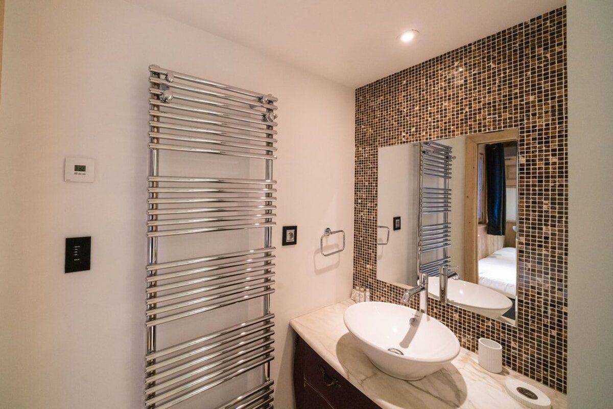 Stylish bathroom with a chrome towel warmer, vessel sink on marble, and a mosaic tiled wall with a mirror reflecting a room.