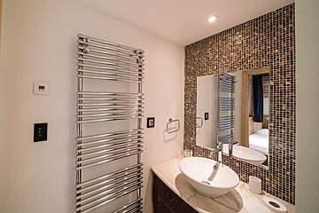 Modern bathroom with a white vessel sink, a mosaic tile wall behind the mirror, and a large chrome heated towel rack.
