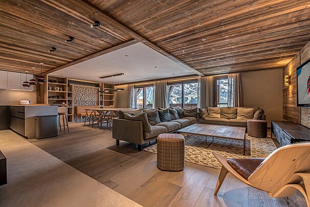 Cozy, modern chalet interior: open-plan living, dining, kitchen, with warm wood, stylish furnishings & snowy mountain views.