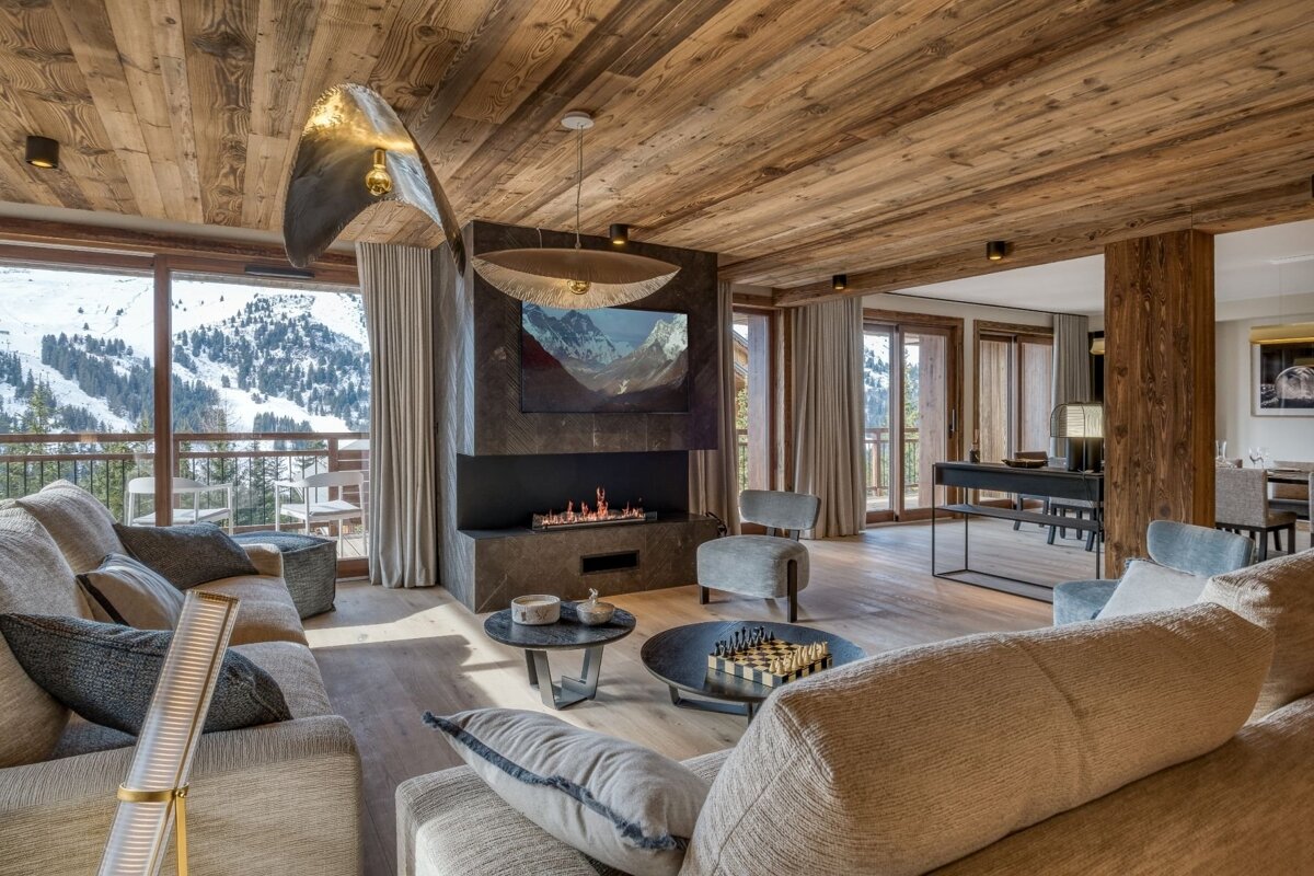 Luxurious ski chalet living room with a snowy mountain view, rustic wood ceilings, modern fireplace, and comfortable furnishings.