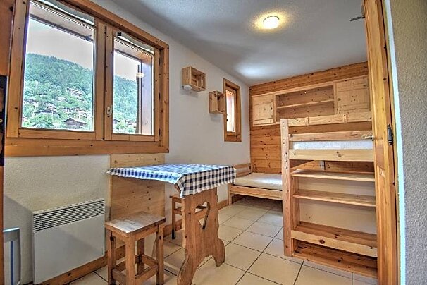 A cozy wooden cabin room with bunk beds, a dining table with a checkered tablecloth, and a view of mountains through the window.