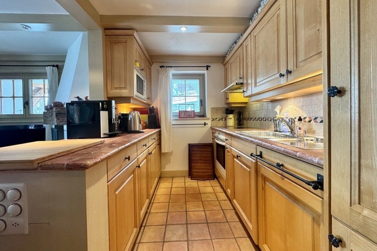 Cozy galley kitchen with light wooden cabinets, tiled floors, and a small window at the end.