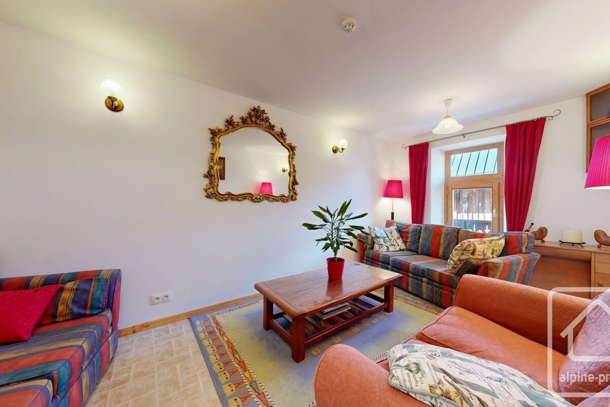 A cozy living room with colorful striped sofas, a wooden coffee table, an ornate gold mirror, red curtains and lamps, and a potted plant.