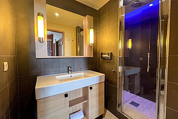 Modern bathroom with a wooden sink vanity, mirror with wall lights, and a glass-enclosed shower with blue LED lighting.