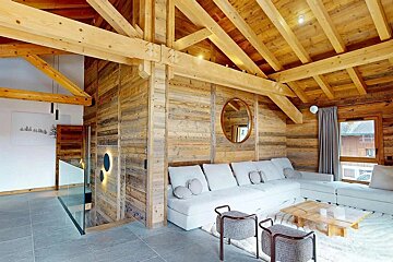 Cozy chalet living room with exposed wood beams, a large white sectional sofa, rustic walls, and a modern aesthetic.
