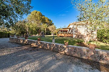A stone wall surrounds a lush green yard with a house in the background