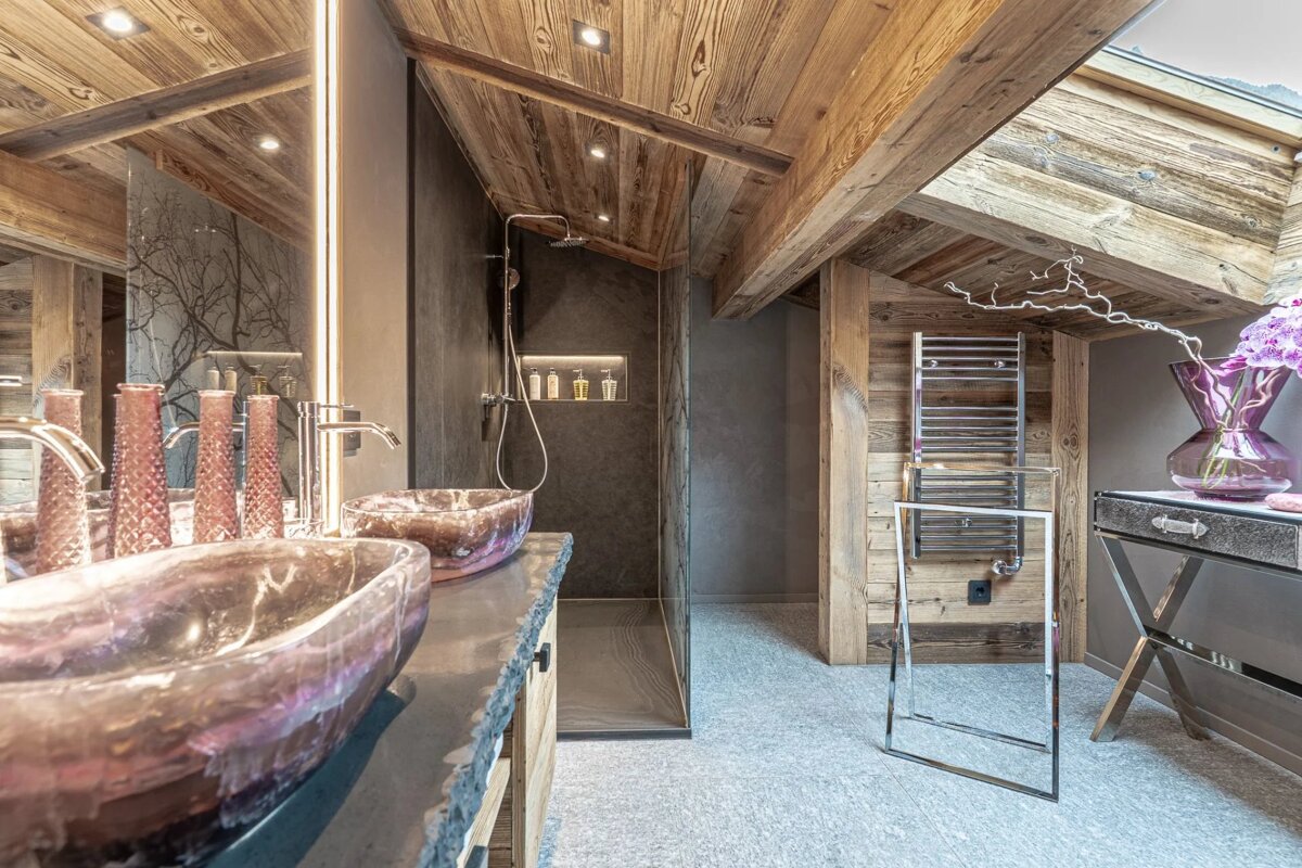 Modern chalet-style bathroom featuring slanted wooden ceilings, a walk-in shower, and purple glass vessel sinks.